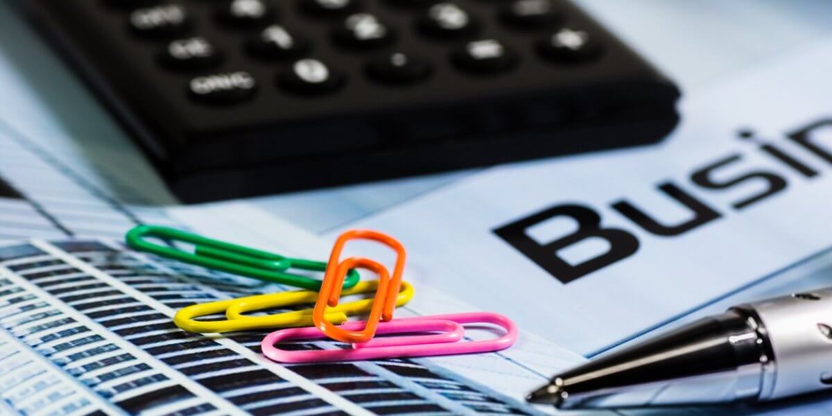 Calculator, colorful paper clips, and a pen resting on financial documents labeled "Business" with a focus on financial analysis tools.