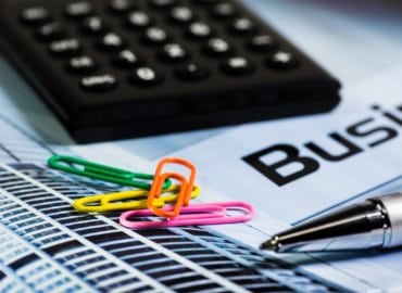 Calculator, colorful paper clips, and a pen resting on financial documents labeled "Business" with a focus on financial analysis tools.