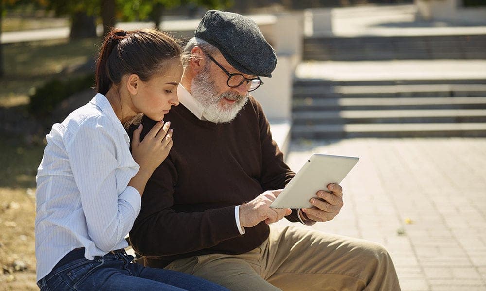 Help someone you love. Portrait of young smiling girl sitting with grandfather and laptop against city park. community and family lifestyle concept