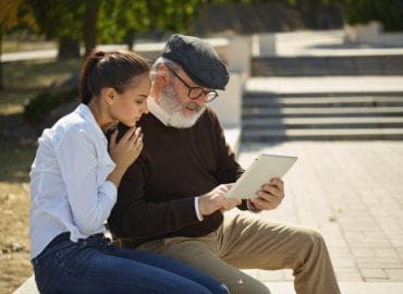 Help someone you love. Portrait of young smiling girl sitting with grandfather and laptop against city park. community and family lifestyle concept