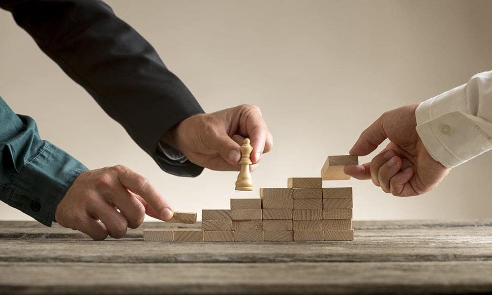 Business teamwork concept with a businessman moving a chess piece queen up a series of steps formed by blocks being put in place by his team.