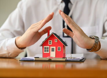 Man hands protecting over little house.