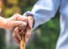 Close up of elderly hands in wrinkles holding walking stick. elderly old man with walking stick stand on footpath sidewalk crossing.