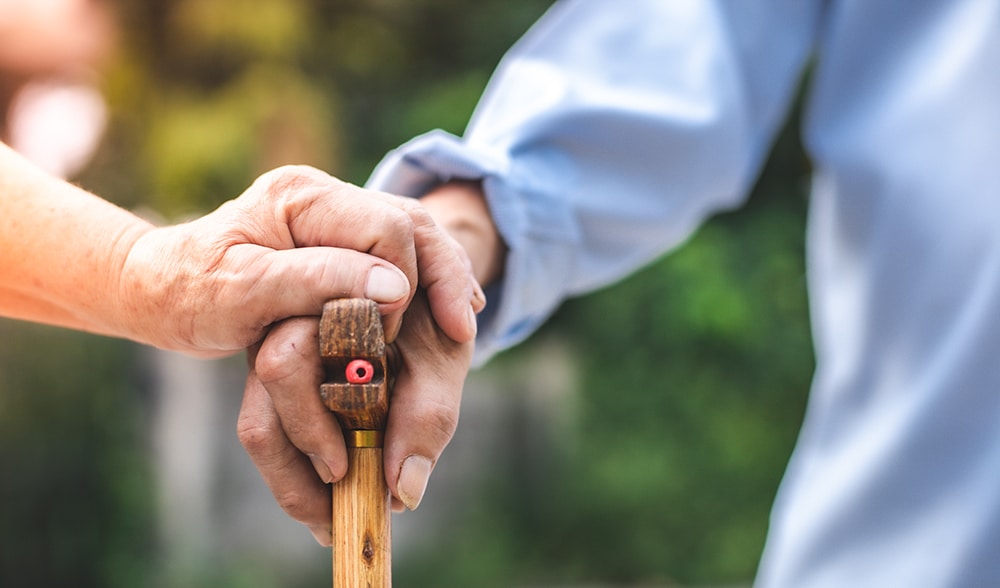 Close up of elderly hands in wrinkles holding walking stick. elderly old man with walking stick stand on footpath sidewalk crossing.