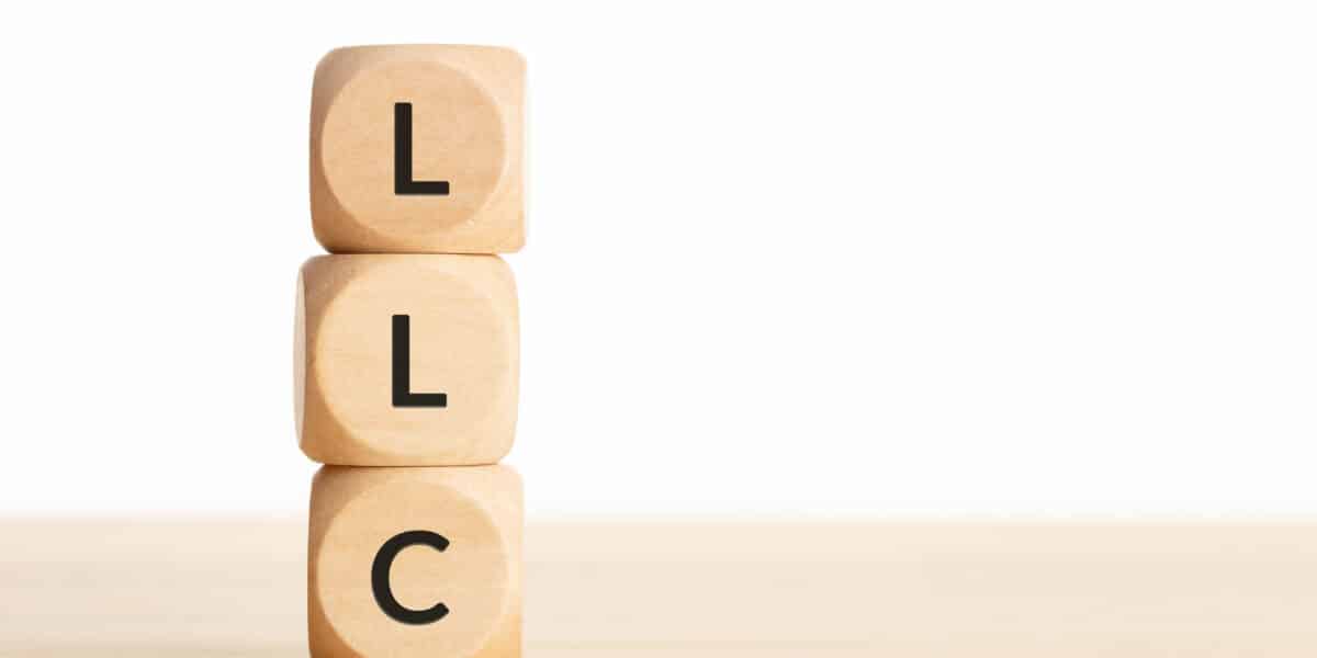 Three wooden blocks stacked vertically, each with a black letter, starting from the top: "L", "L", "C" against a plain white background. The blocks rest on a light wooden surface, symbolizing how LLCs can protect your assets with simplicity and strength.