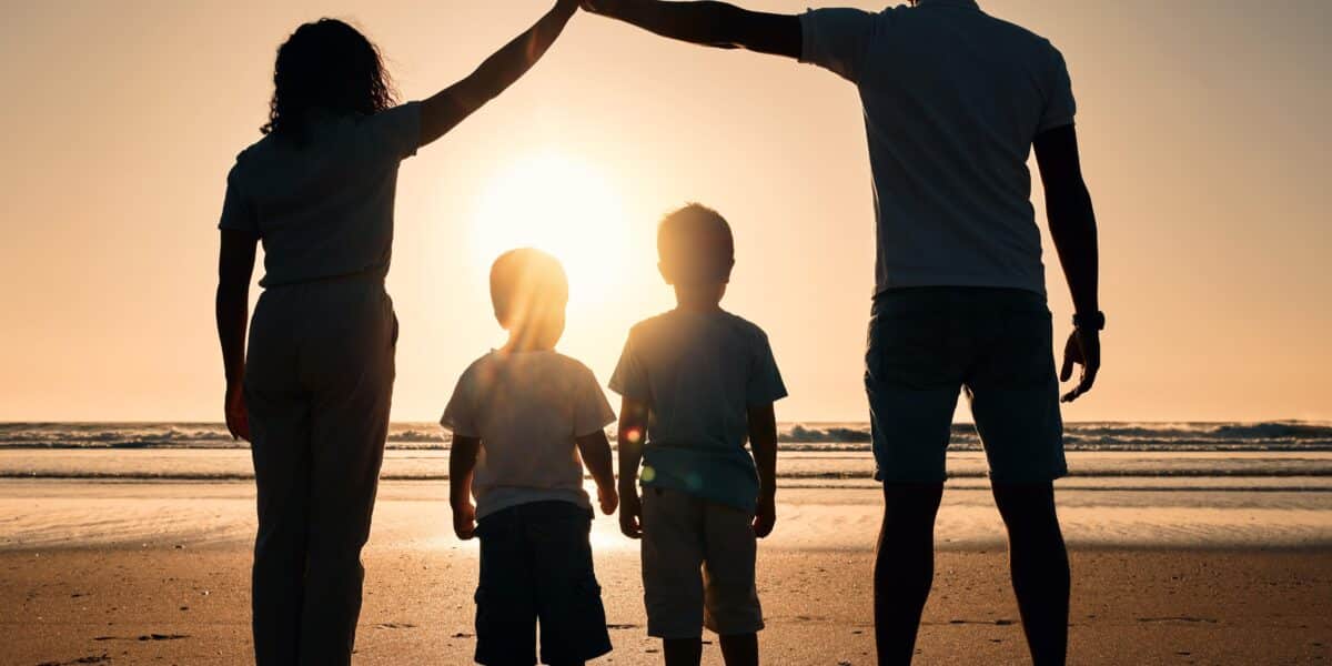 A silhouetted family of four—two adults and two children—stands on a beach at sunset, celebrating the moment with a high five. Like estate planning tools that secure futures, they share timeless bonds while facing the vast ocean together.