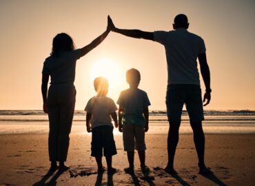 A silhouetted family of four—two adults and two children—stands on a beach at sunset, celebrating the moment with a high five. Like estate planning tools that secure futures, they share timeless bonds while facing the vast ocean together.